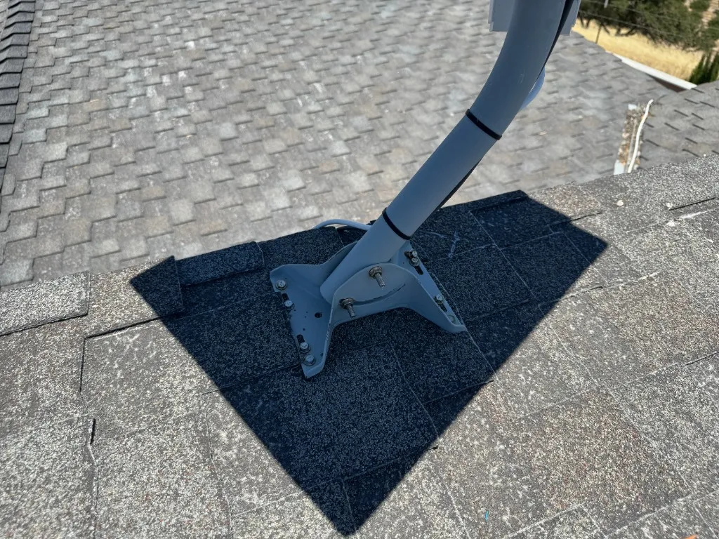 Antenna mount bolted directly to an asphalt shingle roof, with bolts and fasteners visible on the mounting bracket