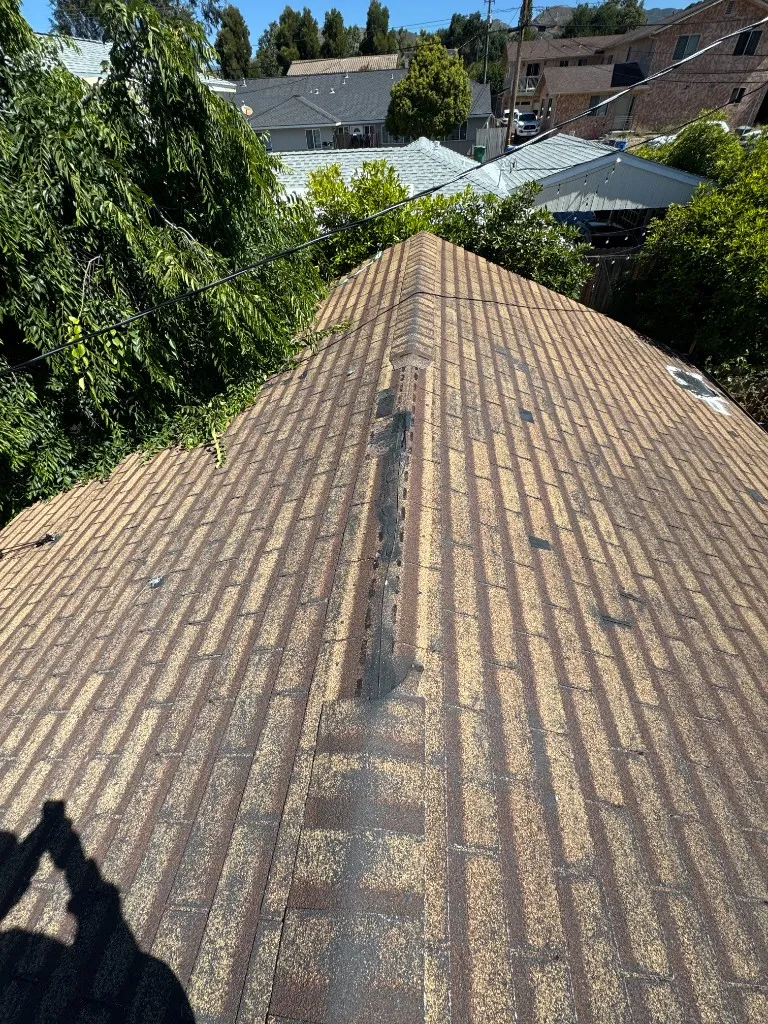 Asphalt shingle roof with weathered, worn shingles and a section of the ridge cap missing along the peak
